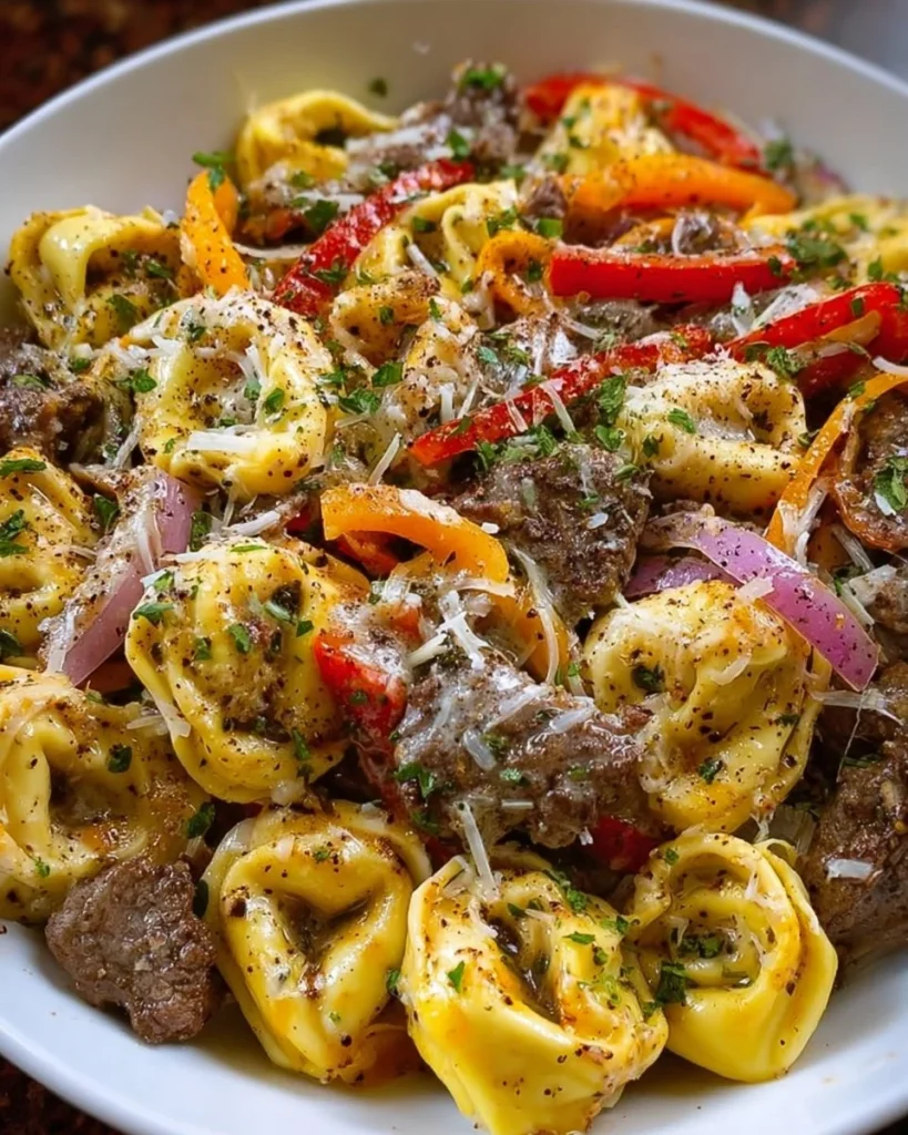 Crock Pot cheesesteak tortellini served in a bowl with cheese and herbs.