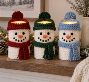 Three crochet snowman covers on flameless LED pillar candles with colorful hats and scarves