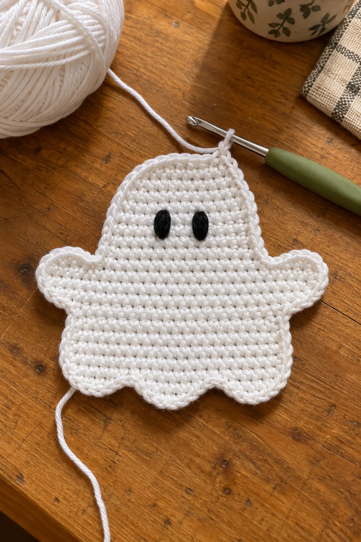 Flat white crochet ghost topper in progress with embroidered black eyes.